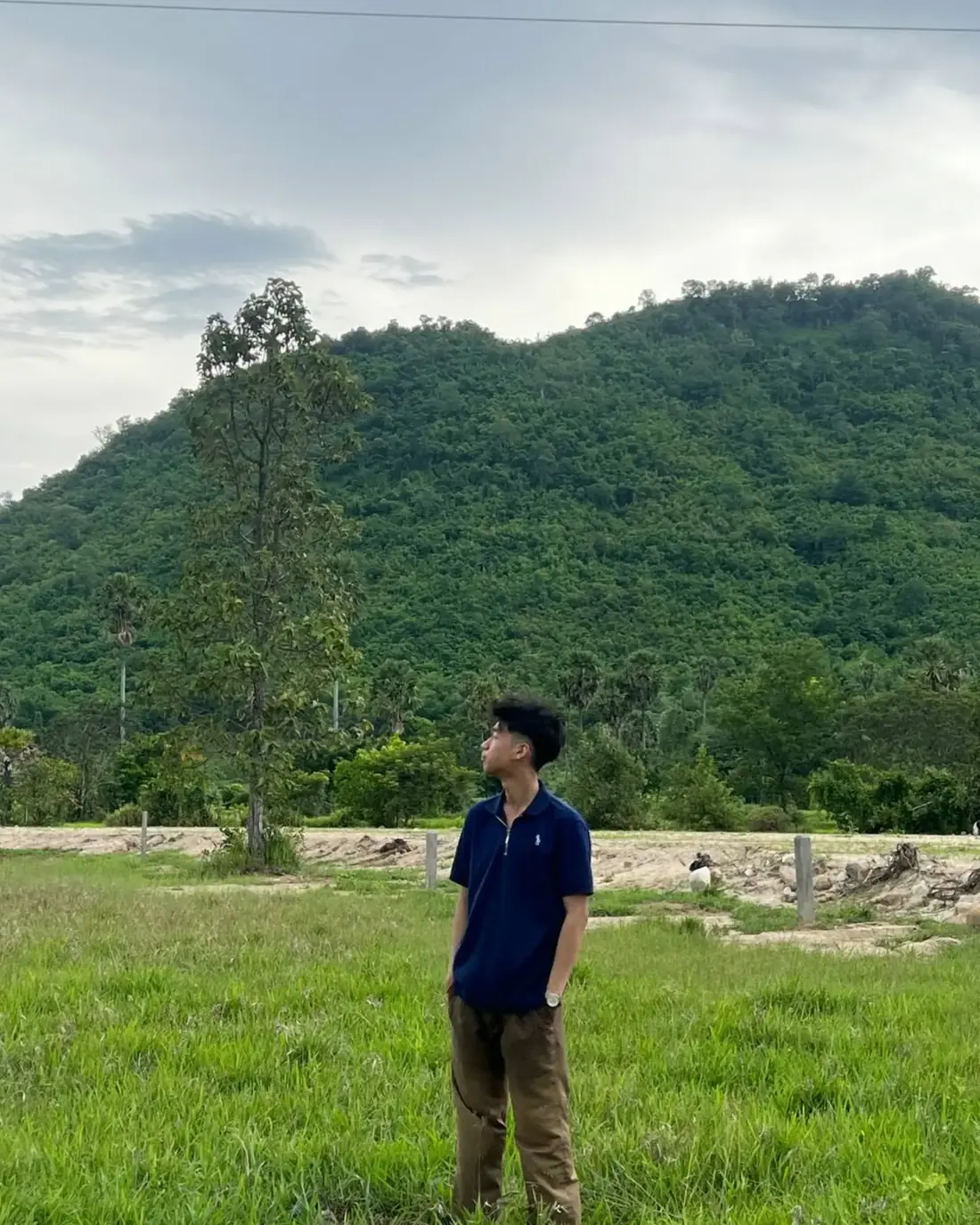 Seng Thay standing in a green field, looking up at forested hills