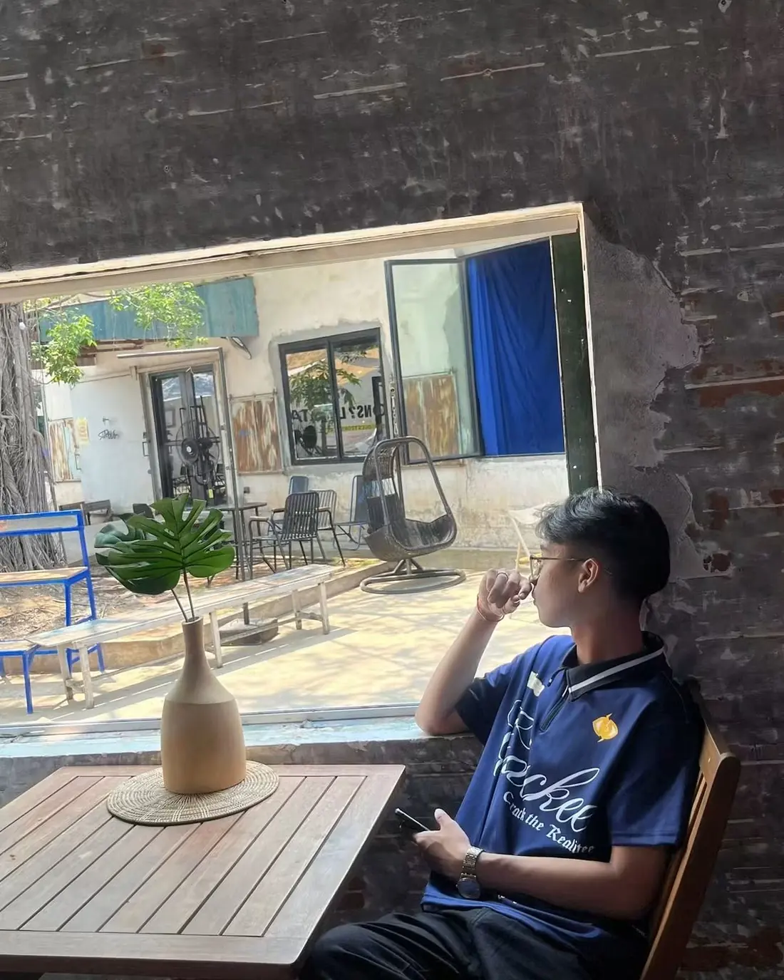 Seng Thay seated at a café window, looking out at a sunlit courtyard