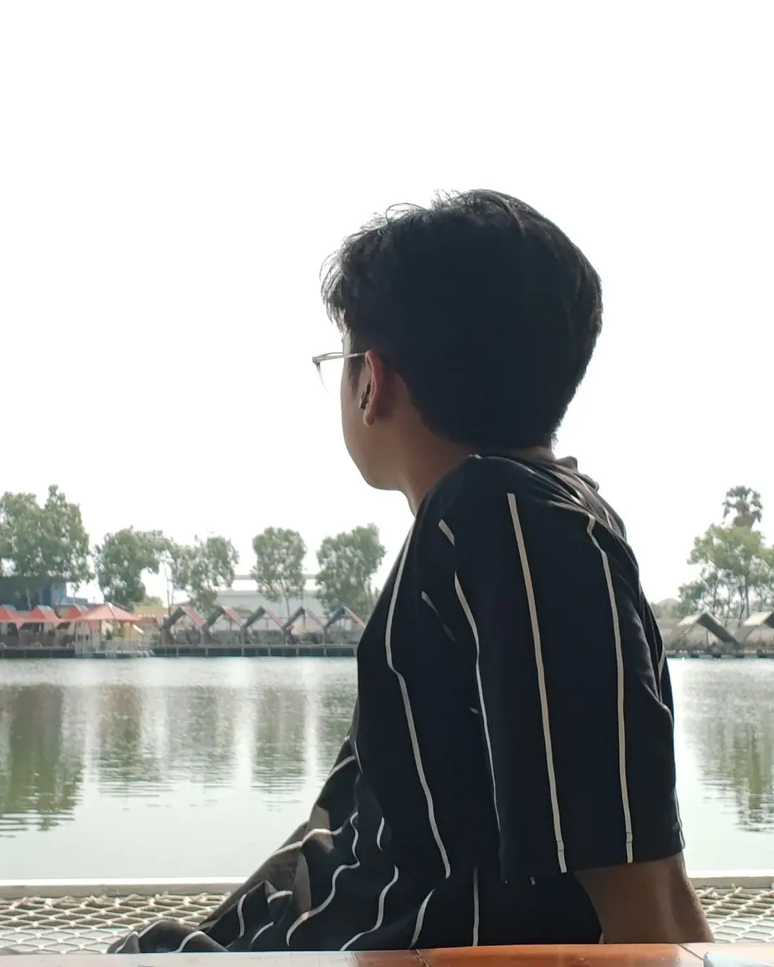Seng Thay in profile looking across a calm lake toward red-roofed huts