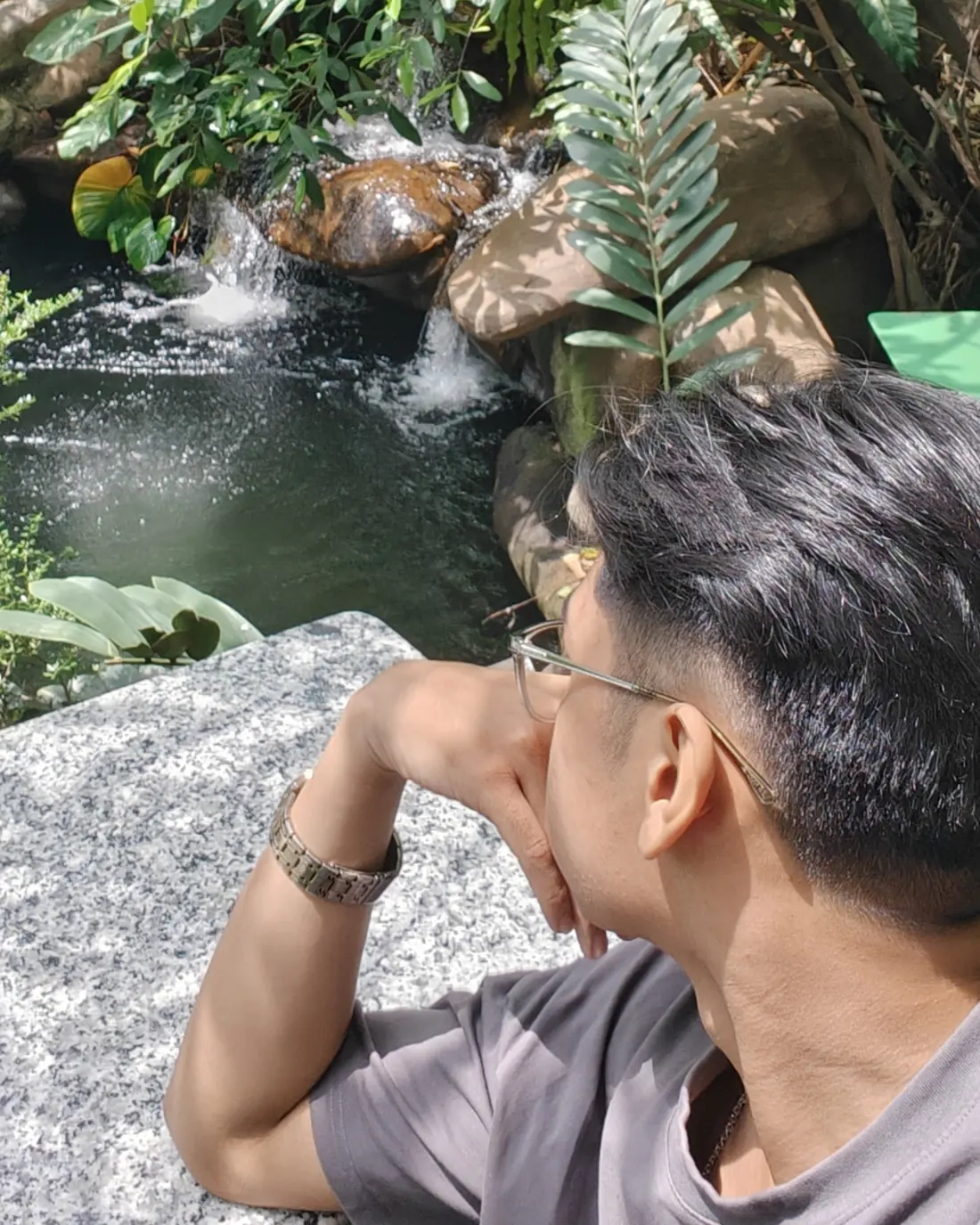 Seng Thay resting on a stone ledge beside a garden waterfall